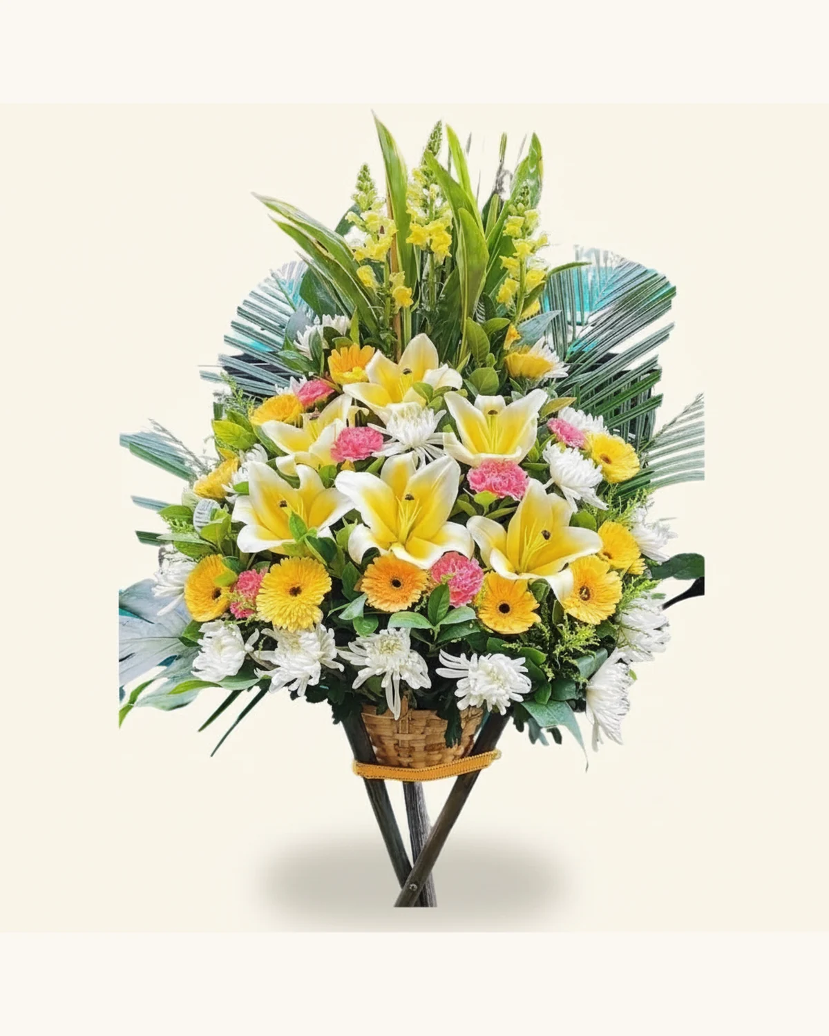 暖意追思站立花籃 — 黃色及白色百合樣花朵、黃色雛菊形花朵、粉紅色球狀花朵、白色多瓣菊樣花朵、黃色細小簇狀花朵、深綠葉材及藍綠色扇形裝飾葉片、棕色藤編花籃、深色交叉支架及金黃色絲帶