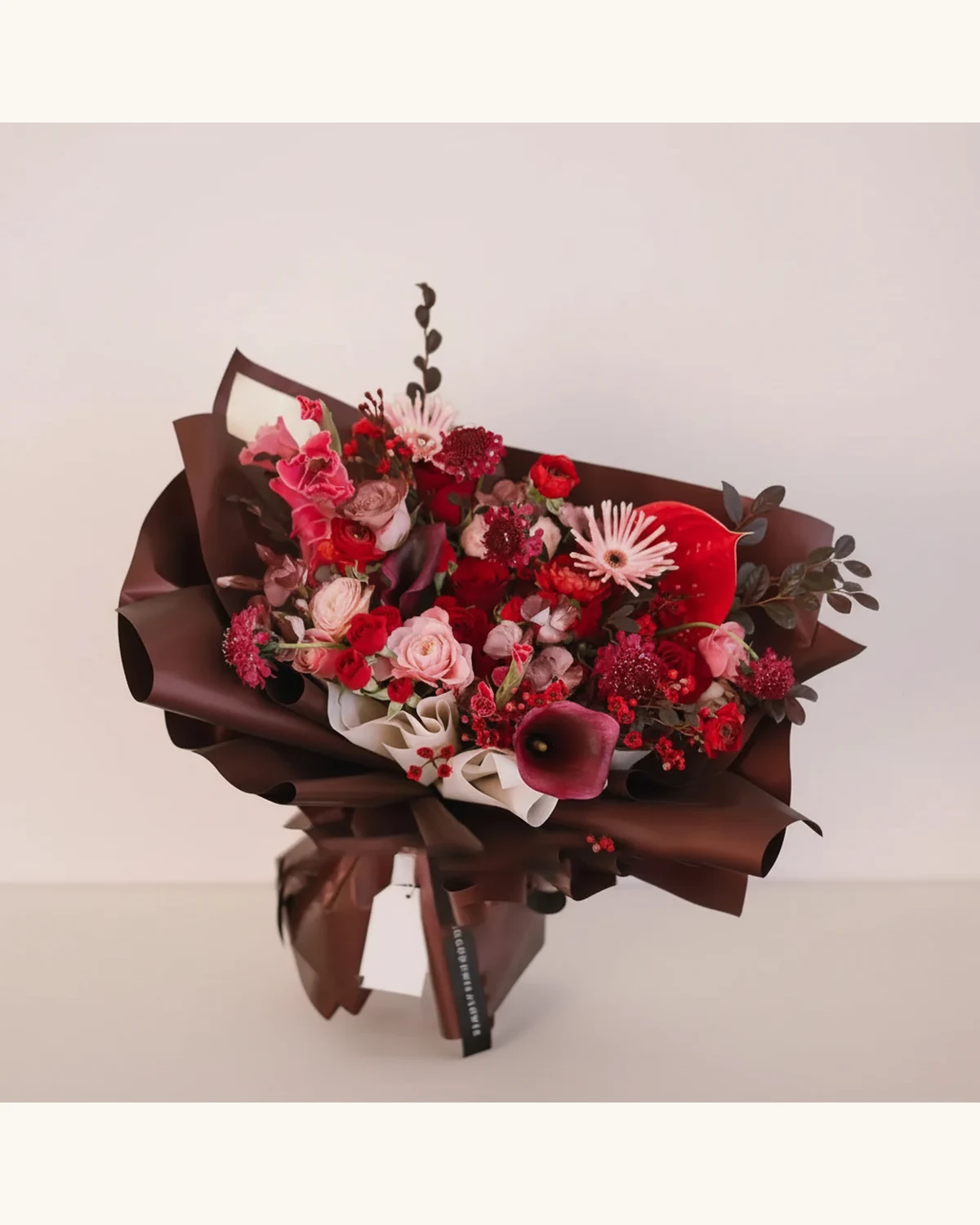 Red and Pink Rose Christmas Bouquet — Red Roses, Pink Roses, Anthurium, Gerbera, Calla Lily, Carnations, Wax Flowers, Olive Leaves, Dark Brown Wrapping Paper